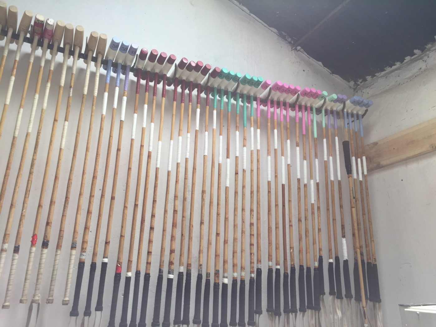 Polo mallets racked on the wall, colour-coded by length